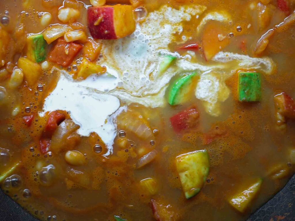 adding coconut milk to pan of pumpkin curry